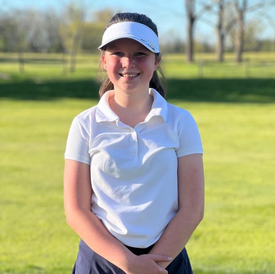 Rylee standing outdoors with a white visor and a big smile