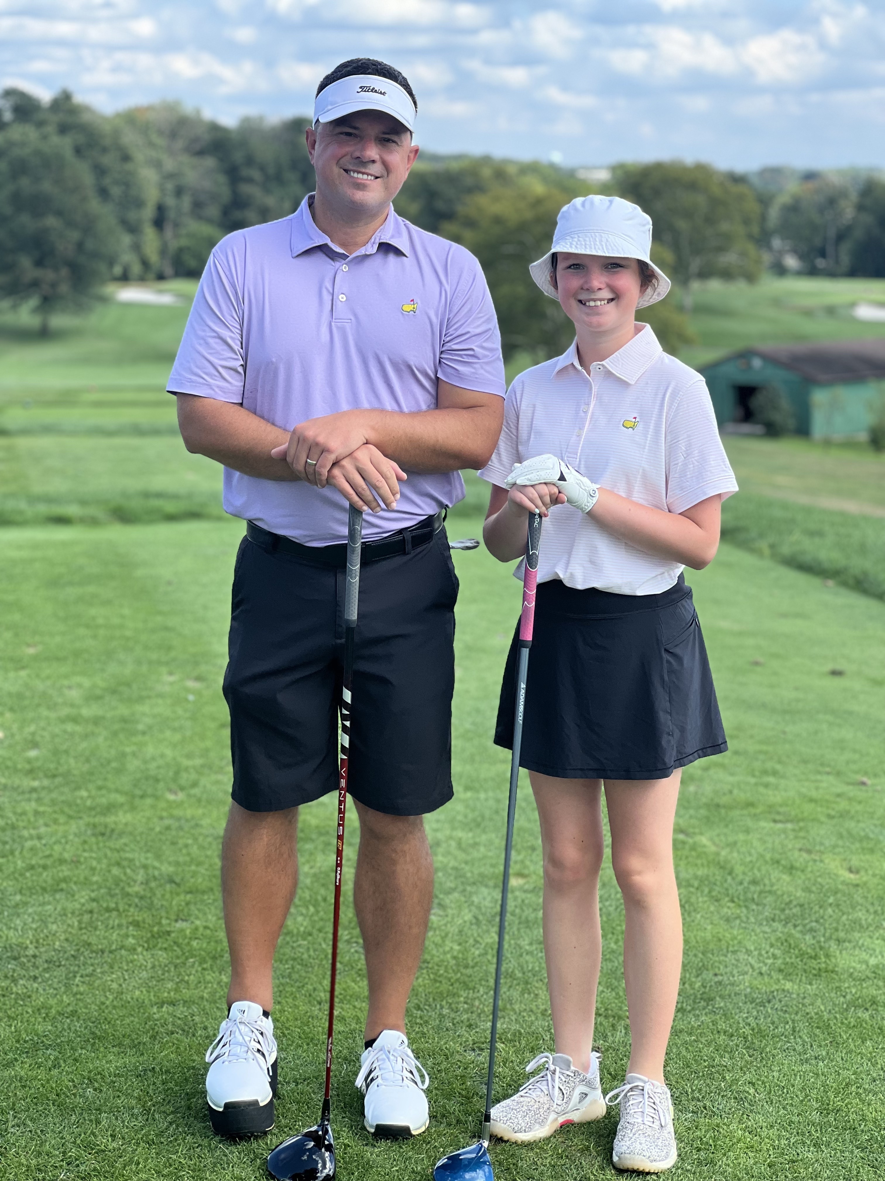 Rylee and Ryan smiling while posing with their clubs at a golf-course